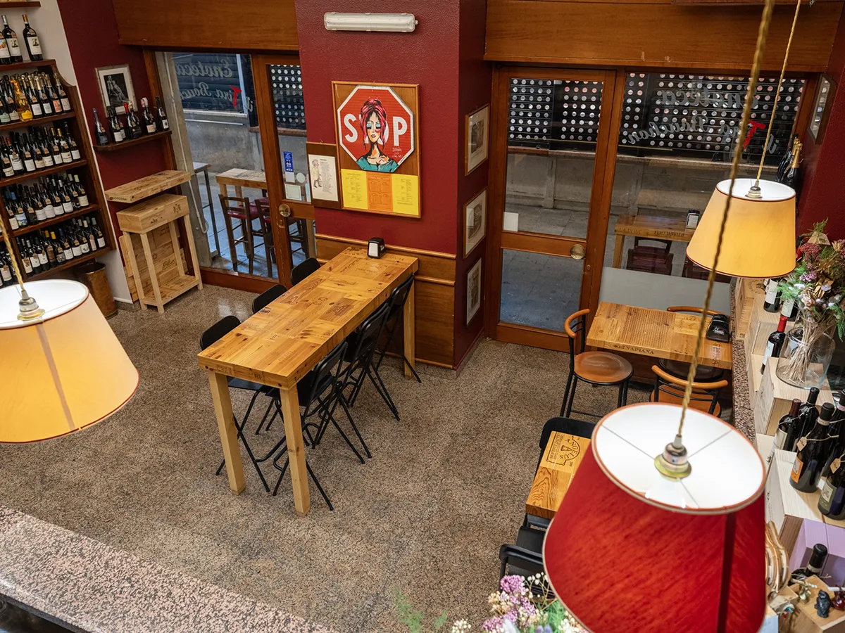 Vista interna dell’enoteca con tavoli, bancone e lampade rosse